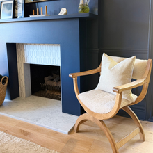 Load image into Gallery viewer, Wooden armchair with white cushions in front of a blue fireplace.