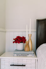 Load image into Gallery viewer, two candle holders on books on nightstand with flowers and bed on side